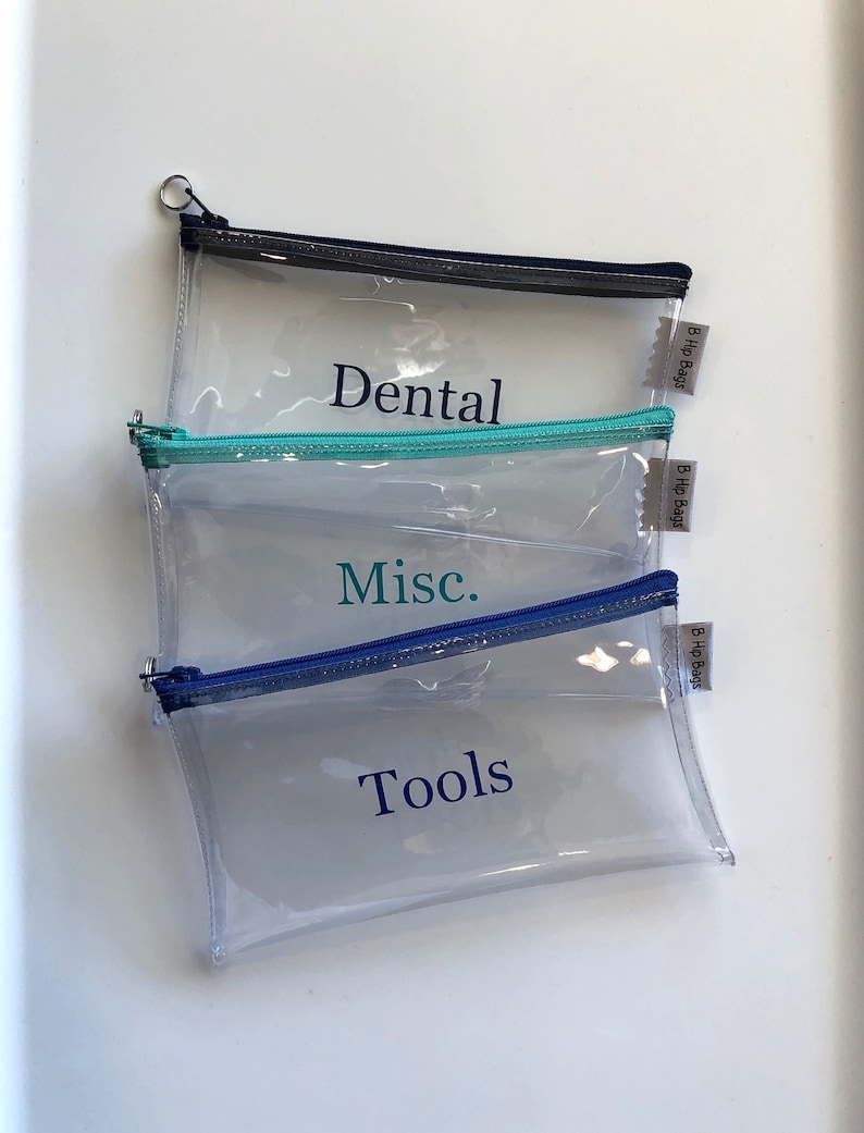 May include: Three clear plastic zippered pouches with blue, teal, and gray zippers. The pouches are labeled "Dental", "Misc.", and "Tools" in blue text. Each pouch has a small white label with the text "B Hip Bags" on it.