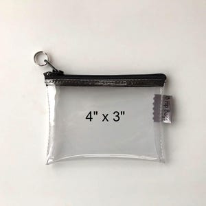 May include: A clear plastic zipper pouch with a black zipper and a silver ring pull. The pouch is 4 inches by 3 inches and has a label that says "B Hip Bags".