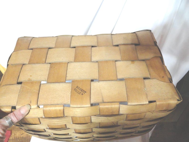 May include: A woven basket made of natural materials with a light brown color. The basket has a rectangular shape and is made with a woven pattern. The text "Basket Ville" is printed on the bottom of the basket.