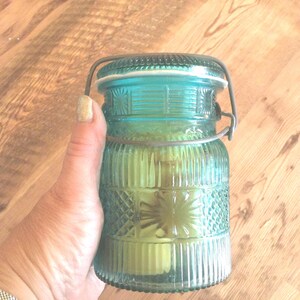 May include: A teal blue glass jar with a wire bail closure. The jar has a textured, ribbed design and a white rim.