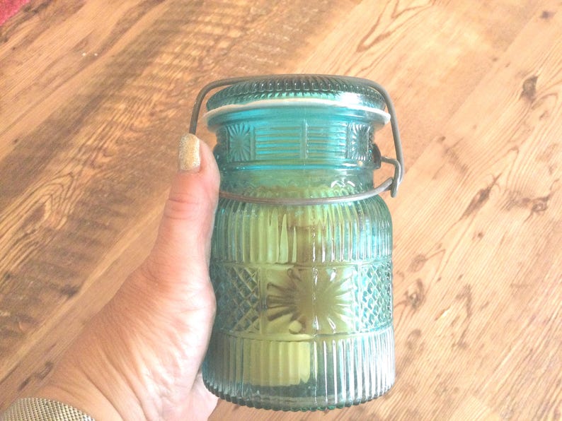 May include: A teal blue glass jar with a wire bail closure. The jar has a textured, ribbed design and a white rim.