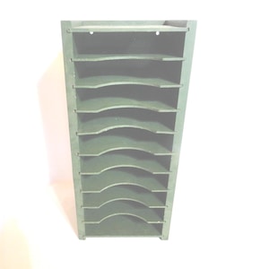 May include: A dark green wooden organizer with multiple curved shelves. The organizer has a rectangular shape and is designed to hold items. The shelves are evenly spaced and provide storage. The item is made of wood and has a simple design.
