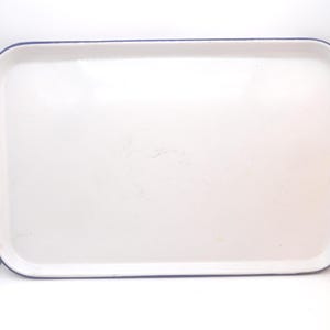 May include: A rectangular serving tray with a smooth white surface and a dark blue rim. The tray features rounded corners and a slightly raised edge, providing a clean and simple design for carrying items. The finish appears glossy and uniform.