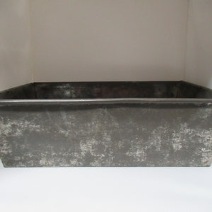 May include: A rectangular metal planter with a distressed gray finish. The planter has a slightly raised rim and a smooth, flat bottom.
