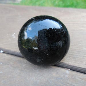 May include: A black glass sphere with a smooth, shiny surface. The sphere reflects light and has a slight shimmer.