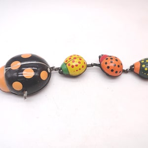 May include: A vintage-style metal pull toy featuring a large black ladybug with orange spots connected to three smaller, colorful ladybugs in yellow, orange, and dark green, each decorated with contrasting spots and linked by metal hinges.