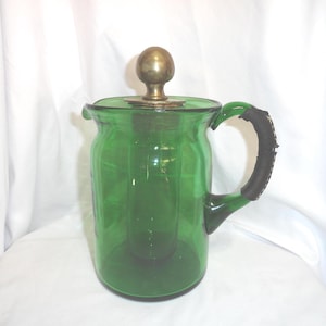 Pode incluir: Uma jarra de vidro verde com uma tampa de latão e uma alça de couro.