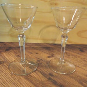 May include: Two clear glass stemmed cocktail glasses with a fluted design. The glasses are empty and sitting on a wooden surface.