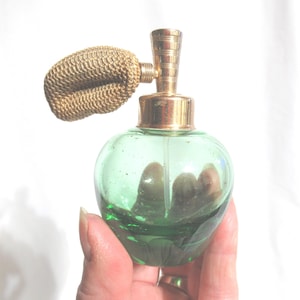 May include: A vintage green glass perfume bottle with a gold atomizer and a gold mesh top. The bottle is shaped like an apple.