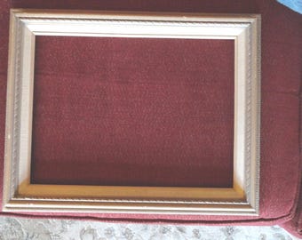 May include: A simple, plain, gold-colored picture frame with a slightly raised edge. The frame is on a burgundy fabric surface.