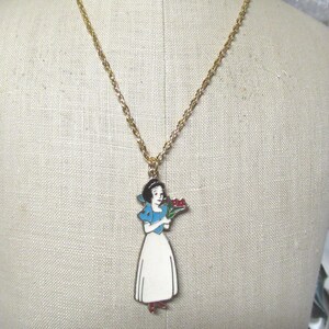 May include: A gold chain necklace with a pendant featuring Snow White in a blue dress holding a bouquet of red flowers.