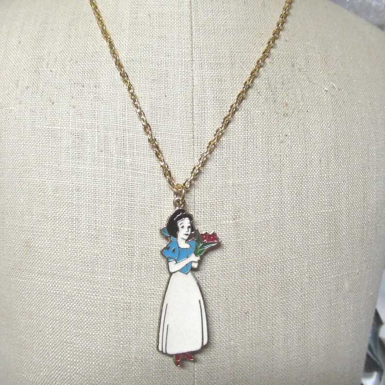 May include: A gold chain necklace with a pendant featuring Snow White in a blue dress holding a bouquet of red flowers.