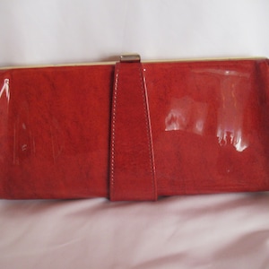 Cartera pequeña vintage de vinilo naranja quemado, estilo años 60, tipo sobre, o con asa de metal en tono dorado, con aspecto de charol retro