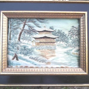 May include: A framed picture of a Japanese pagoda in a snowy landscape. The pagoda is a traditional wooden structure with a curved roof and multiple tiers. The snow is depicted in white and blue tones, creating a serene and peaceful scene.