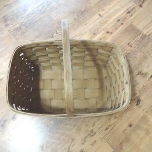 May include: A woven wooden basket with a handle. The basket is empty and has a rectangular shape.