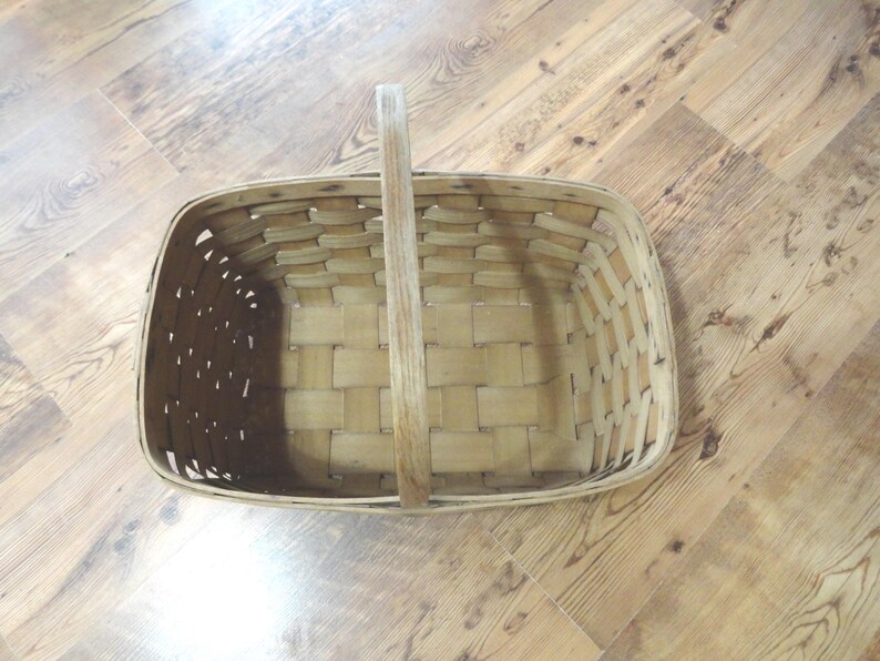 May include: A woven wooden basket with a handle. The basket is empty and has a rectangular shape.