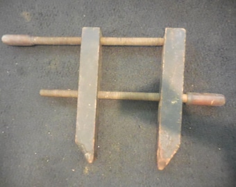 May include: A wooden clamp with two metal screws. The clamp is made of dark wood and has a simple design.