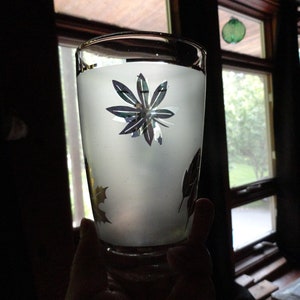 May include: A frosted glass with a silver floral design. The glass is partially filled with a white liquid.
