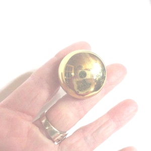 May include: A shiny, gold-colored, spherical object. The surface reflects the surrounding environment. The object is held in a hand, and a gold ring is visible on a finger.