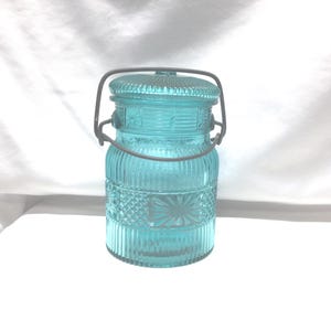 May include: A vintage blue glass jar with a wire handle. The jar has a textured design and is perfect for storing food or other items.