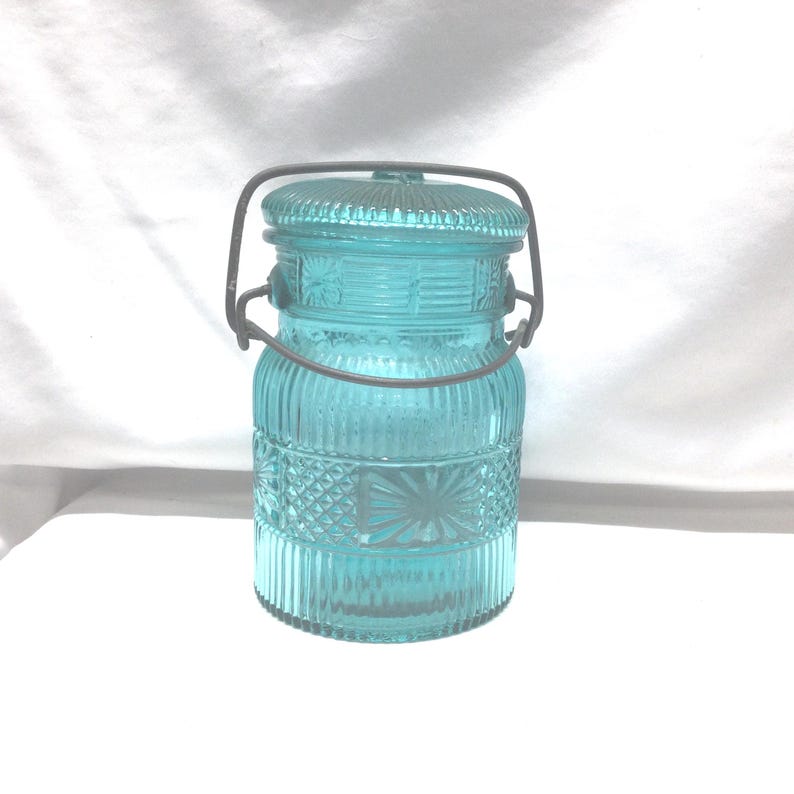 May include: A vintage blue glass jar with a wire handle. The jar has a textured design and is perfect for storing food or other items.