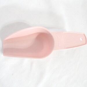 May include: A light pink plastic scoop with a curved bowl and a long handle. The handle has a small hole at the end. The scoop is designed for kitchen use, likely for measuring or serving dry goods.