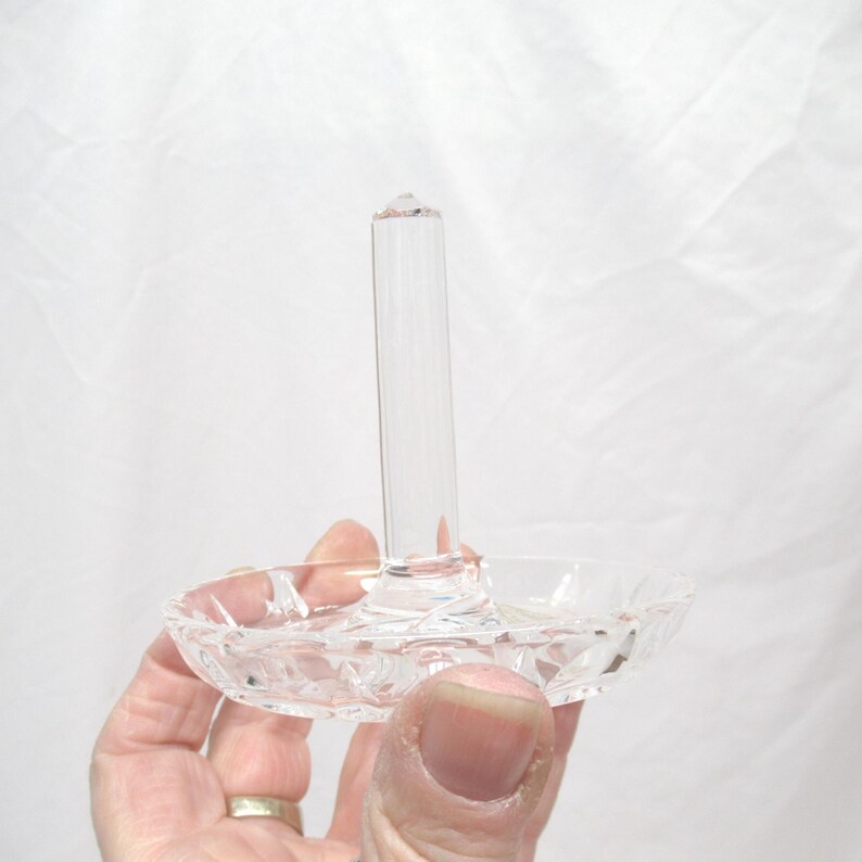 Op de afbeelding: Transparante glazen ringhouder met een lange, cilindrische paal en een kleine, ronde basis. De basis heeft een decoratief, geslepen glaspatroon. De ringhouder is ontworpen om ringen en andere kleine sieraden te presenteren.