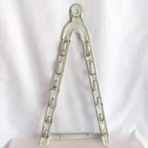 May include: A white metal triangular rack with multiple hooks for hanging items. The rack has a rounded top with a small hole in the center. The rack is designed to be mounted on a wall.