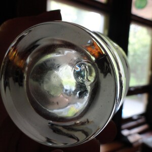 May include: The bottom of a clear glass bottle with a round, smooth base. The glass is thick and has a slight green tint.