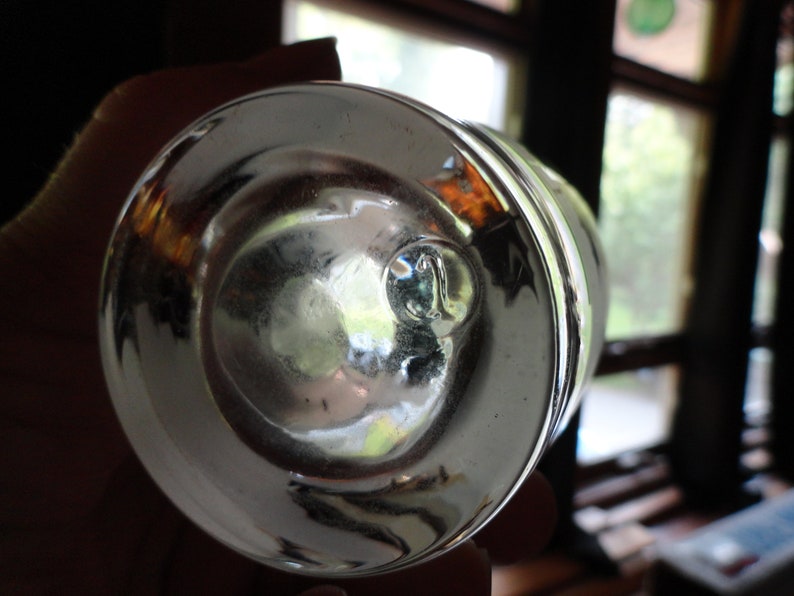 May include: The bottom of a clear glass bottle with a round, smooth base. The glass is thick and has a slight green tint.