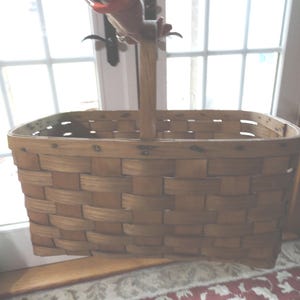 May include: A large, oval-shaped, woven basket with a wooden handle. The basket is made of natural wood and has a rustic, vintage look.