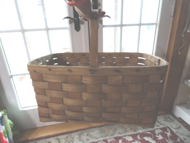 May include: A large, oval-shaped, woven basket with a wooden handle. The basket is made of natural wood and has a rustic, vintage look.