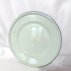 May include: A white enamel plate with a blue rim. The plate has a slight green tint and shows signs of wear.