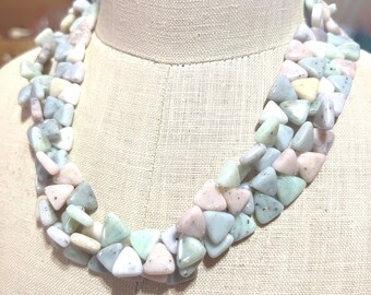 May include: A multi-strand necklace made of triangular green, pink, and white stones. The necklace is displayed on a fabric-covered mannequin.