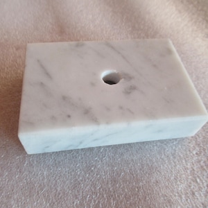 May include: A white marble base with a round hole in the center. The base is smooth and has a light gray veining pattern.