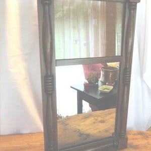 May include: A vintage wooden framed mirror with a rectangular shape and a dark brown finish. The mirror has two sections, one above the other, and is in good condition.