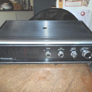 May include: A black vintage Panasonic AM/FM radio with woodgrain trim. The radio has a silver face with tuning knobs, volume, tone, and selector knobs.