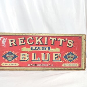 May include: A vintage wooden box with a red label that reads "Reckitt's Paris Blue" in gold lettering. The label also features a crown logo and the text "Reg. U.S. Pat. Off." and "Contains 1/15 Pound".