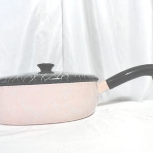 May include: A pink and black enamel saucepan with a black handle and a white swirl design.
