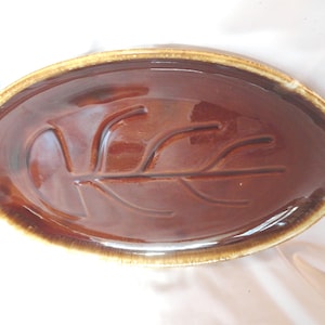 May include: A brown oval ceramic serving platter with a leaf design. The platter has a brown glaze with a light brown rim.