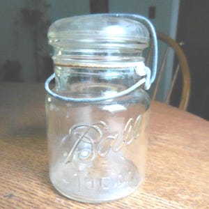 May include: A clear glass Ball jar with a wire bail handle. The jar has a white label with the word "Ball" printed on it.