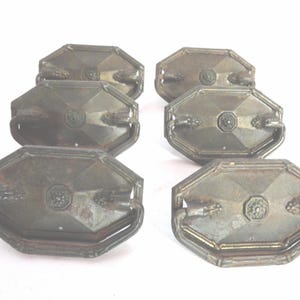 May include: Six antique bronze-toned drawer pulls. Each pull has an octagonal shape with a central floral design and decorative handles. The pulls are arranged in two rows of three against a white background.