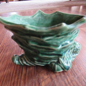 May include: A green ceramic planter shaped like a stylized tree trunk with a wide, shallow bowl. The planter has a textured surface and is designed to hold small plants.