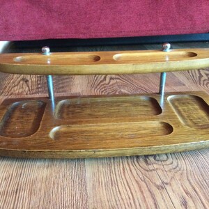 May include: A wooden valet tray with four compartments and a top shelf. The tray is brown and has a smooth finish. The top shelf is supported by two metal rods with silver-colored ball finials.