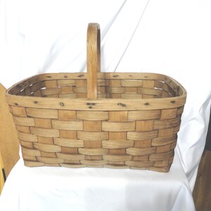 May include: A rectangular wooden basket with a woven design and a single wooden handle. The basket is made of natural wood and has a rustic appearance.
