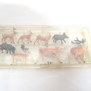 May include: A collection of miniature deer and boar figurines in a clear plastic case. The figurines are painted in shades of brown, tan, and black. The case is rectangular and has a clear lid. The figurines are arranged in rows.