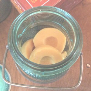 May include: A glass jar with a metal lid and handle, filled with sliced, light brown fruit. The jar is on a wooden surface.