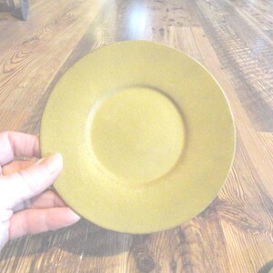 May include: A plain, round, yellow ceramic saucer.