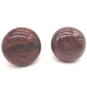 May include: Two polished, spherical stones with a reddish-brown color and a marbled appearance. The stones have a smooth, reflective surface and are set against a white background. The stones appear to be decorative or collectible items.