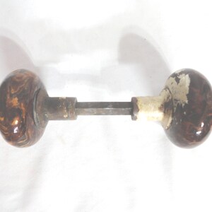 May include: A vintage door knob with a brown and white marbled finish. The knob is attached to a metal rod.